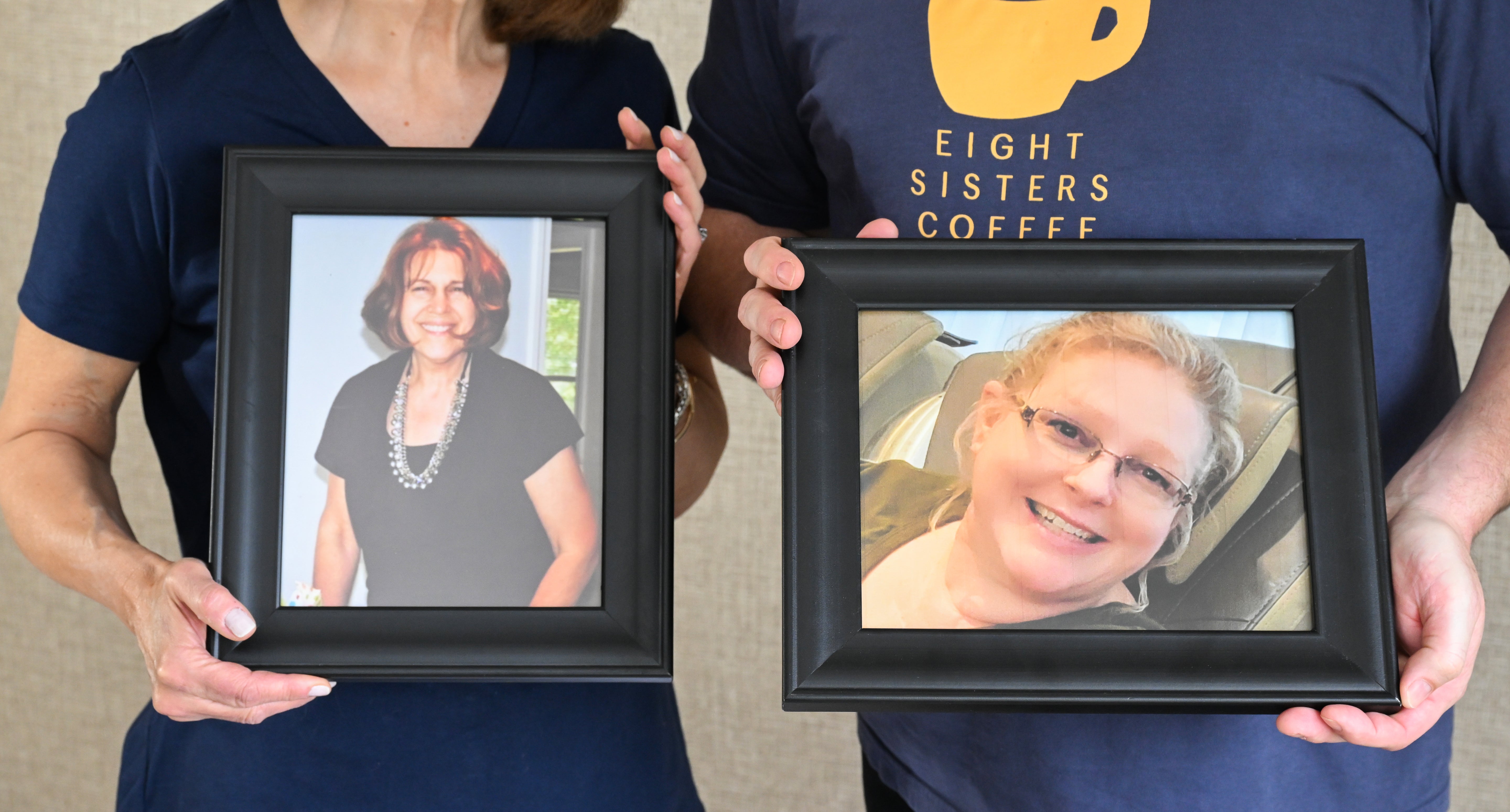 Two people holding framed pictures of women, one with 'Eight Sisters Coffee' shirt.