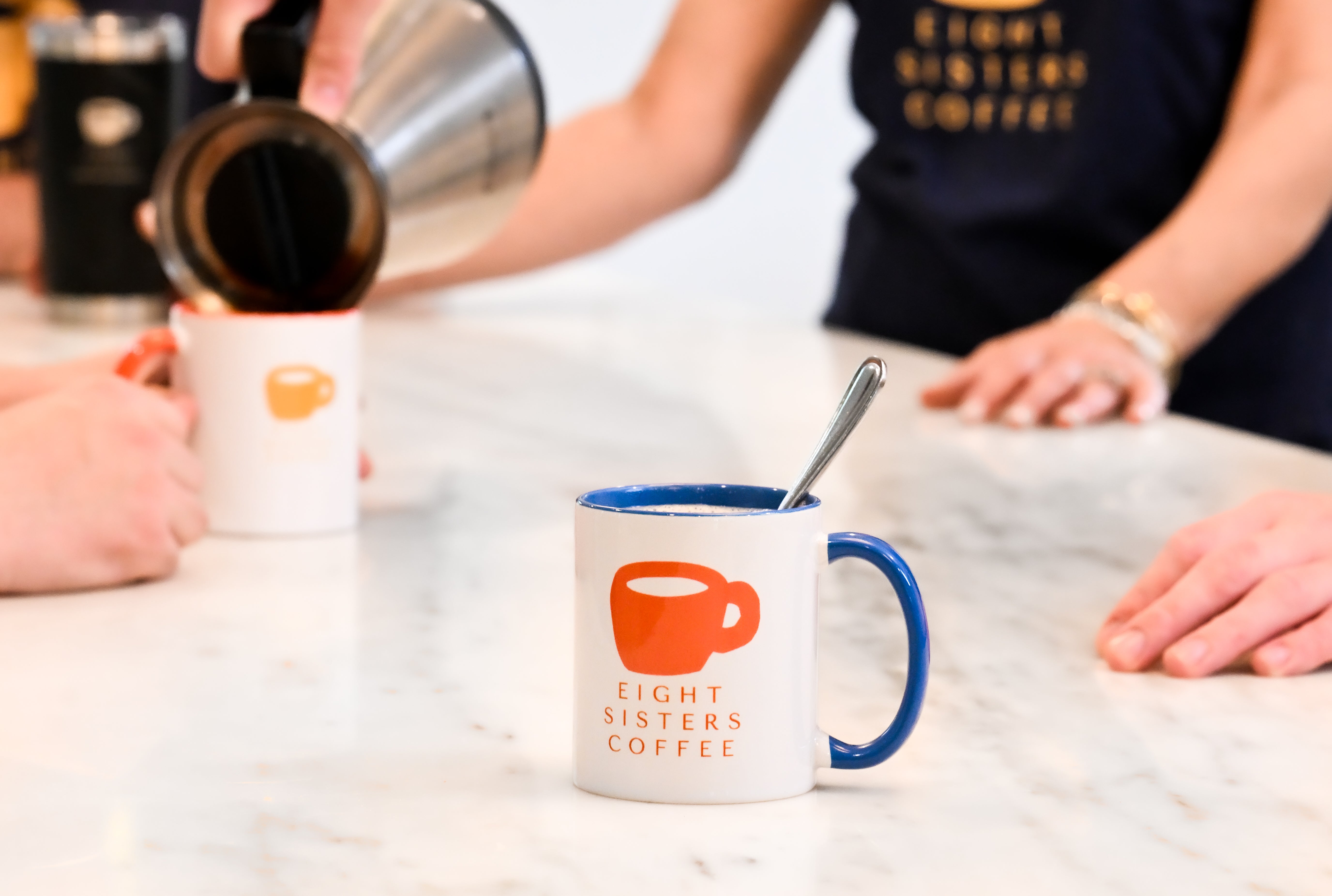 Person pouring coffee into a mug with 'Eight Sisters Coffee' branding on a marble surface.