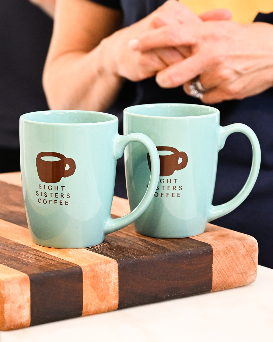 Two light blue mugs with 'Eight Sisters Coffee' logo on a wooden cutting board.